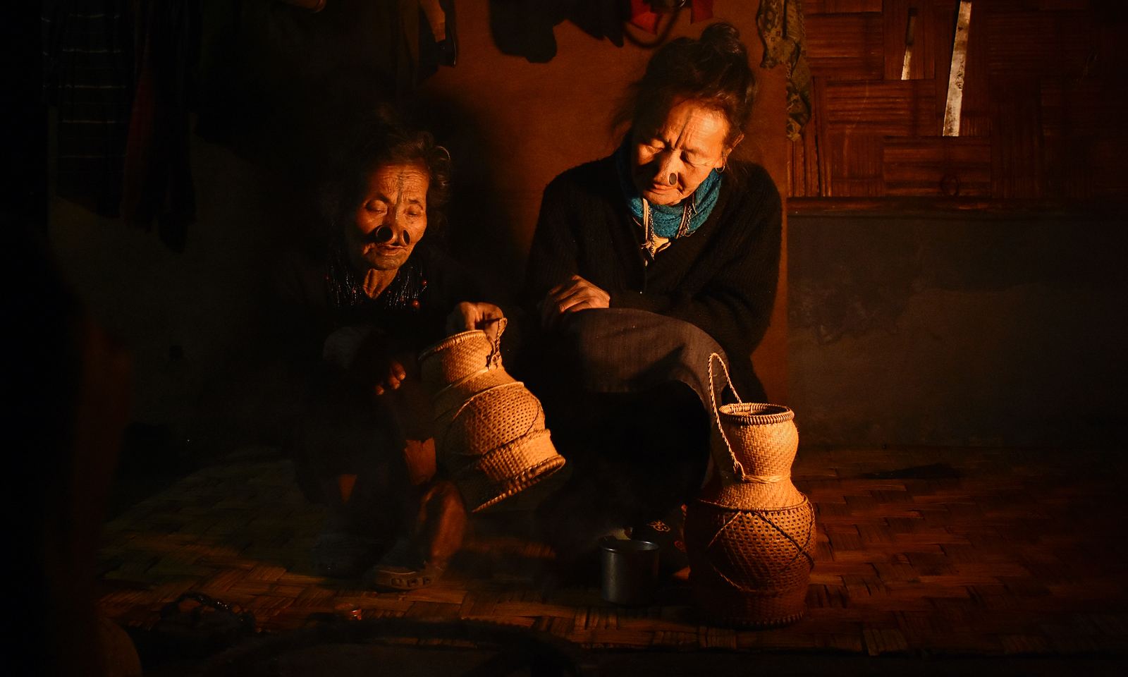 Two Apatani women sitting by the fire in a dark wooden house